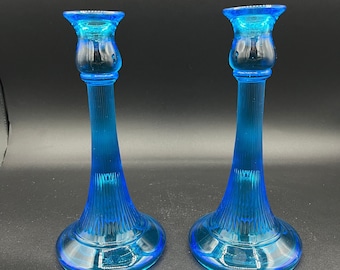 May include: A pair of blue glass candle holders with a fluted design. The holders have a wide base and a narrow top.