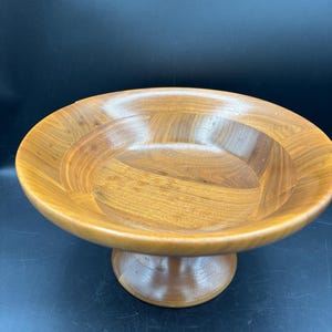 May include: A wooden bowl with a pedestal base. The bowl is made of light brown wood and has a smooth, rounded shape.