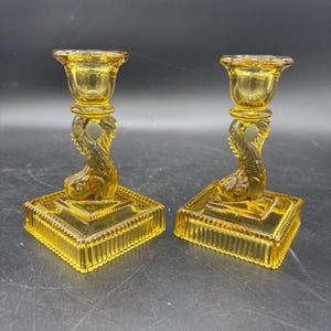 May include: A white ceramic mug with a black handle and the text "But First, Coffee" in a bold, black font. The mug is set against a neutral background, highlighting its simple design. The mug appears to be approximately 4 inches tall.