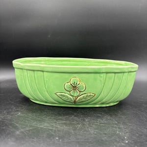 May include: A light green ceramic planter with a ribbed design. The oval-shaped planter features a gold-accented floral design on the front. The planter is suitable for indoor or outdoor use.