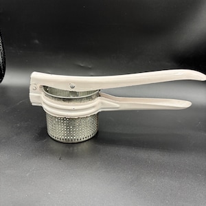 May include: A white metal potato masher with a stainless steel mashing cup. The masher has a long handle and a spring-loaded mechanism.