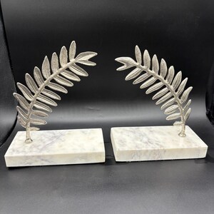 May include: A pair of silver leaf bookends with white marble bases. The leaves are stylized and have a delicate, elegant look.