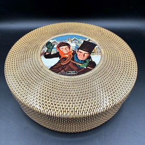 May include: A round, brown and tan wicker-style box with a circular image of a man and child in a winter scene. The image is surrounded by a white border.