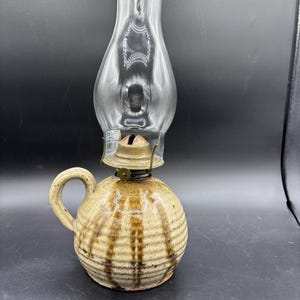 May include: A ceramic oil lamp with a brown and white striped design. The lamp has a glass chimney and a brass burner.