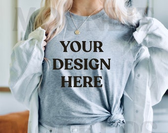 May include: A woman wearing a gray t-shirt with the text "YOUR DESIGN HERE" printed on it. She is wearing a white cardigan and white jeans.