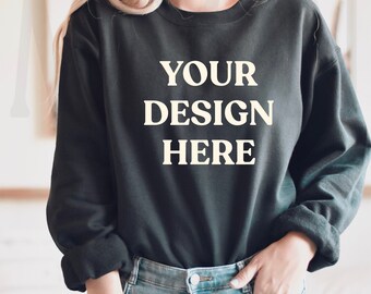 May include: A black sweatshirt with the text "YOUR DESIGN HERE" printed on the front. The sweatshirt is being worn by a person with blonde hair and blue jeans.
