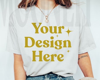May include: A white t-shirt with the text "Your Design Here" in gold lettering with sparkling stars on either side of the text. The model is wearing blue jeans and a brown and white plaid scarf.