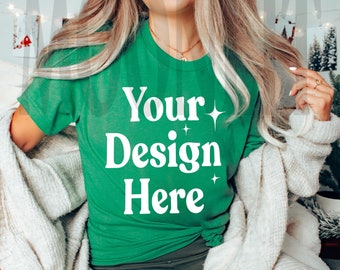 May include: A woman wearing a green t-shirt with the text "Your Design Here" in white. She is sitting on a white blanket with a gold cup and a camera on a tray.