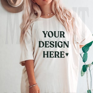 May include: A white oversized t-shirt with the text "YOUR DESIGN HERE" printed on the front. The shirt is being modeled by a person with long blonde hair.
