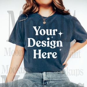 May include: A dark blue t-shirt with the text "Your Design Here" in white, with starburst accents. The model is wearing light blue jeans and white shoes. The shirt is a mockup for custom designs.