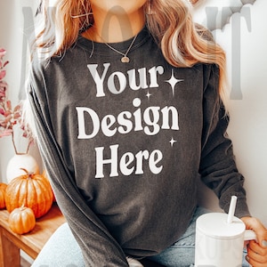 May include: A dark gray long-sleeved shirt with the text "Your Design Here" in white. The shirt has a relaxed fit and is worn by a person sitting on a wooden bench.