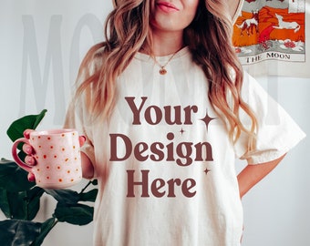 May include: A woman wearing a white oversized t-shirt with the text "Your Design Here" in brown lettering. She is holding a pink polka dot mug.