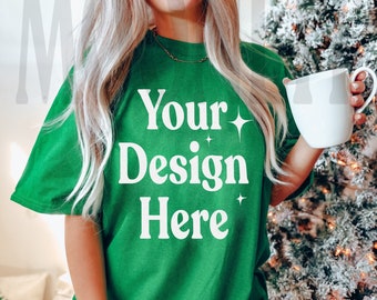 May include: A woman wearing a green oversized t-shirt with the text "Your Design Here" in white. She is holding a white mug and standing in front of a Christmas tree.