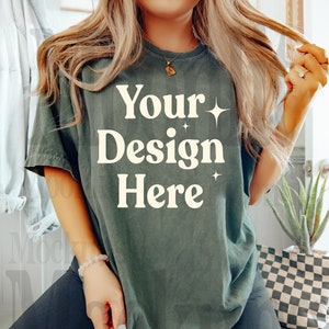 Puede incluir: Una camiseta verde oscuro con el texto "Your Design Here" en blanco con pequeñas estrellas blancas. La camiseta la lleva puesta una persona con el pelo largo y rubio.