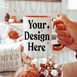 May include: White ceramic mug with an orange rim and handle. The mug has black text that reads "Your Design Here" with small stars on either side of the text.