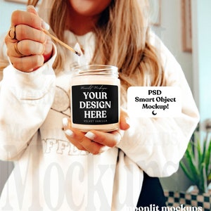 May include: A lit candle in a clear glass jar with a black label that says "YOUR DESIGN HERE" and "VELVET VANILLA". The candle is being lit with a match. The image also includes the text "PSD Smart Object Mockup!"