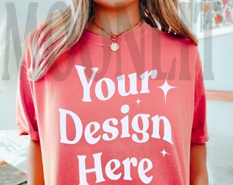 May include: A coral pink t-shirt with short sleeves and a crew neck. The shirt has the text "Your Design Here" printed in white on the front.