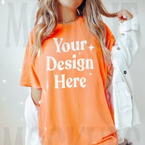 May include: A bright orange oversized t-shirt with the text "Your Design Here" in white. The shirt is being worn by a person with long blonde hair.