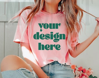May include: A pink t-shirt with the text "your design here" in green letters. The shirt is being worn by a person with long blonde hair and blue jeans.