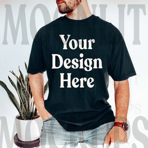 May include: A black t-shirt with the text "Your Design Here" printed in white on the front. The shirt is being worn by a person with a beard and is styled with jeans.