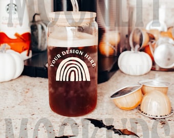 May include: A clear glass jar with a brown lid and a straw, filled with a dark brown liquid. The jar has a white rainbow design with the text "YOUR DESIGN HERE". The jar is sitting on a light brown countertop with a few white pumpkins and coffee pods.