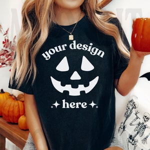 Op de afbeelding: Zwart T-shirt met een wit jack-o'-lantern gezicht en de tekst "your design here" in wit.
