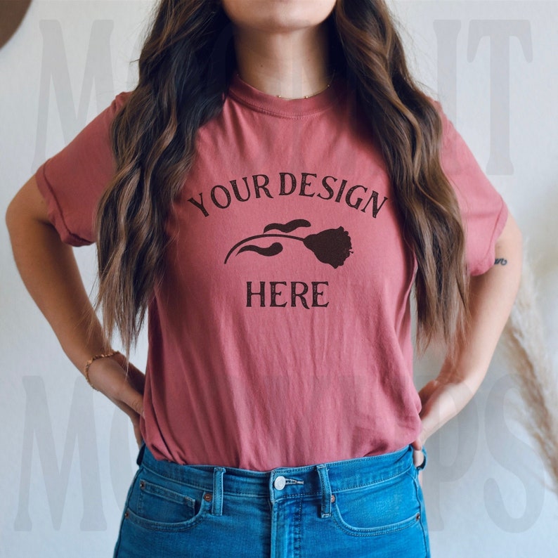 May include: A woman wearing a dusty rose t-shirt with the text "YOUR DESIGN HERE" and a simple flower graphic.