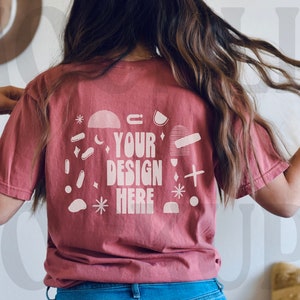 May include: A maroon t-shirt with a white graphic design on the back. The design includes the text "YOUR DESIGN HERE" surrounded by abstract shapes and stars.