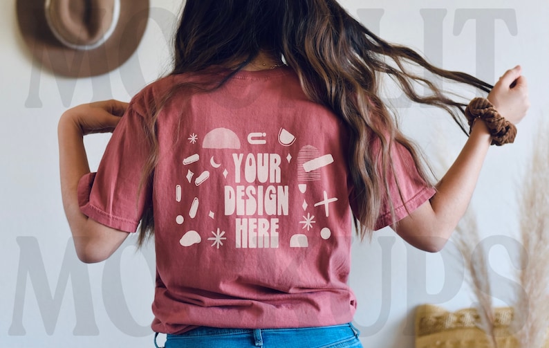 May include: A maroon t-shirt with a white graphic design on the back. The design includes the text "YOUR DESIGN HERE" surrounded by abstract shapes and stars.