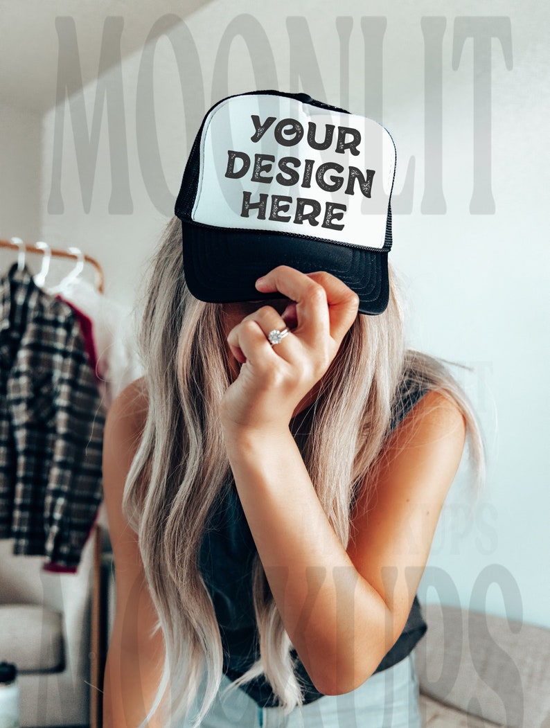 May include: A black and white trucker hat with a mesh back. The hat has the text "YOUR DESIGN HERE" printed on the front.
