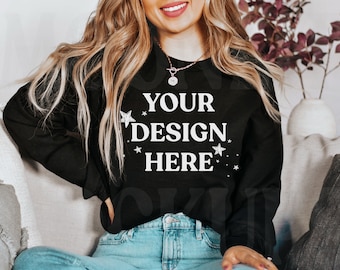 May include: A black sweatshirt with the text "YOUR DESIGN HERE" in white lettering and small white stars around the text. The sweatshirt is being worn by a person sitting on a couch.