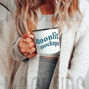 May include: A white enamel mug with a black rim and handle. The mug has the text "moonlit mockups" in blue text with a camera icon.