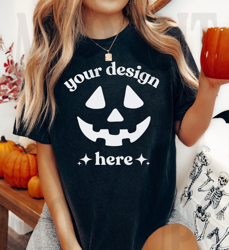 Op de afbeelding: Zwart T-shirt met een wit jack-o'-lantern gezicht en de tekst "your design here" in wit.