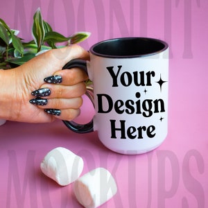 May include: White ceramic mug with a black rim and handle. The mug has the text "Your Design Here" in black with small star accents. The mug is being held by a hand with black and white nail polish.