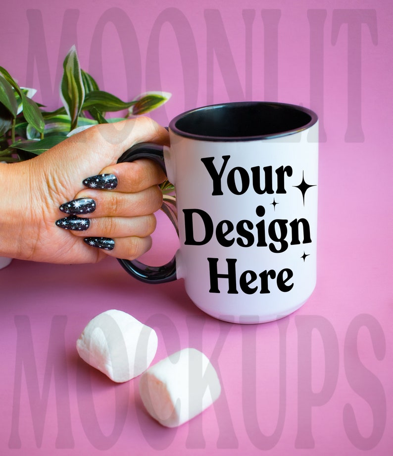 May include: White ceramic mug with a black rim and handle. The mug has the text "Your Design Here" in black with small star accents. The mug is being held by a hand with black and white nail polish.