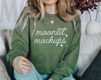 Puede incluir: Una sudadera verde oliva con el texto "moonlit mockups" en blanco, con fuente cursiva. La sudadera la lleva una persona. La imagen es una maqueta para diseños de ropa.