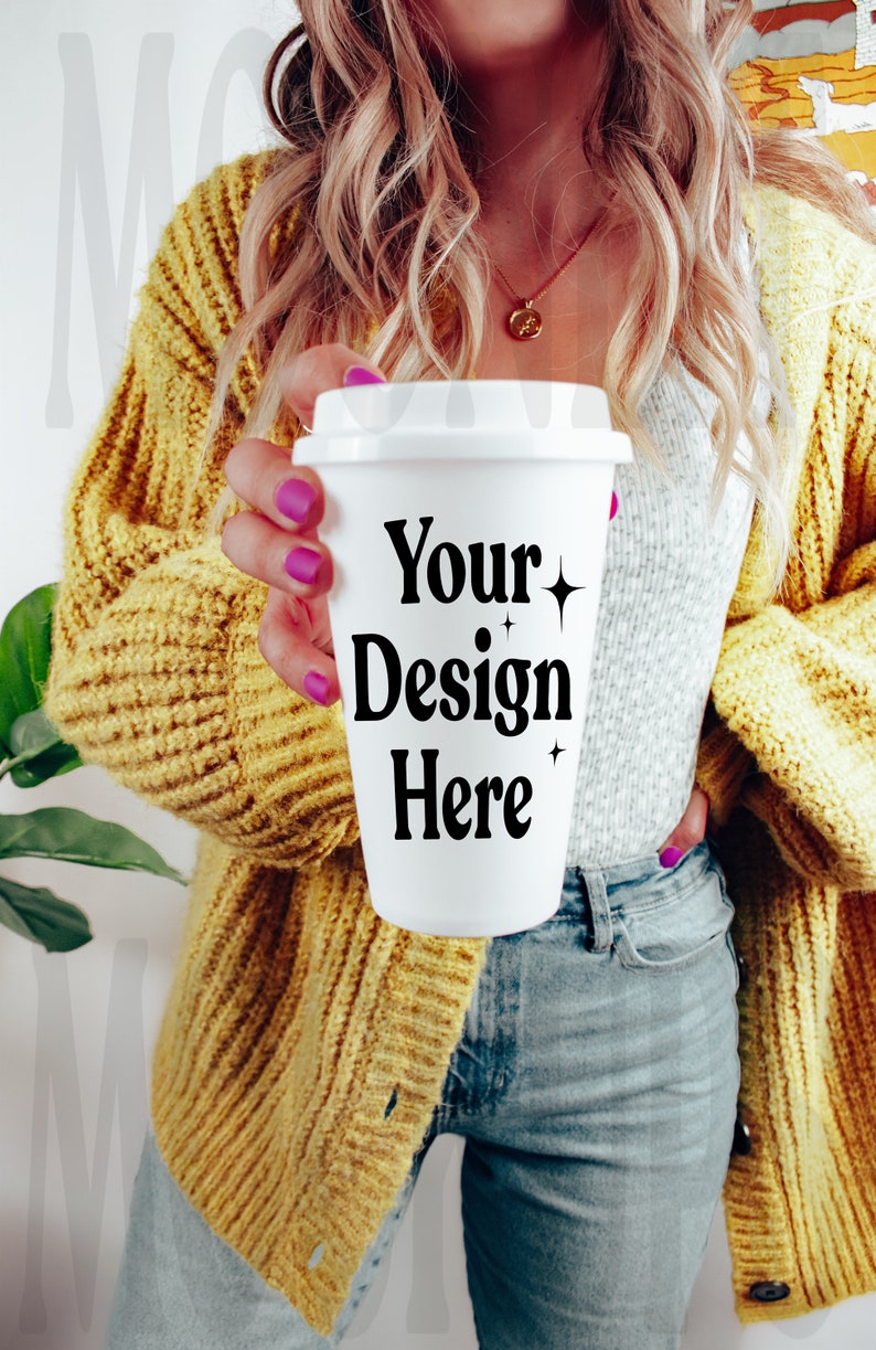 May include: A white to-go coffee cup with a black design that says "Your Design Here". The cup is being held by a person wearing a yellow cardigan and blue jeans.