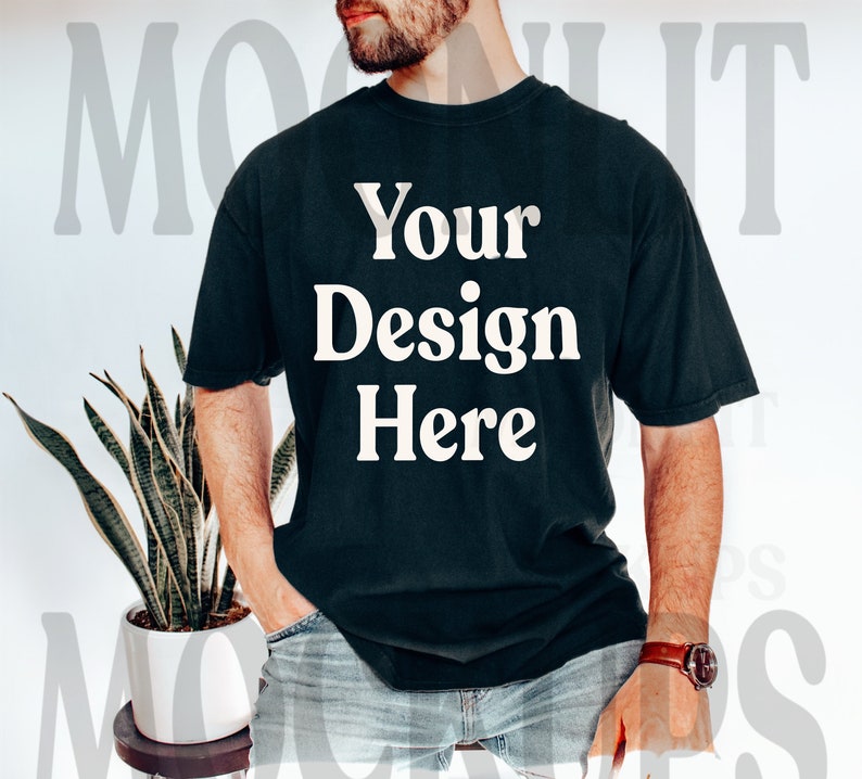 May include: A black t-shirt with the text "Your Design Here" printed in white on the front. The shirt is being worn by a person with a beard and is styled with jeans.
