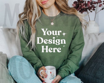 May include: A woman wearing a green sweatshirt with the text "Your Design Here" in white. She is sitting on a sofa and holding a white mug.
