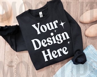 May include: Black sweatshirt with the text "Your Design Here" in white, with small white stars. The sweatshirt is laid out on a wooden surface with a pair of light brown boots and blue jeans.