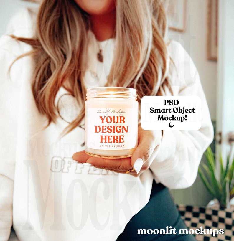 May include: A white candle with a label that says "Your Design Here" and "Velvet Vanilla". The candle is lit and being held by a person. The text "PSD Smart Object Mockup!" is in a speech bubble.