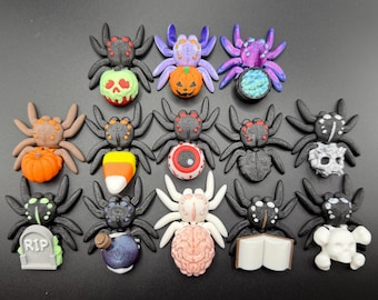 May include: A collection of fourteen small spider figurines arranged in three rows. Each spider features a unique Halloween-themed object, including pumpkins, a skull, a candy corn, an eyeball, a tombstone with RIP text, a brain, and a book.