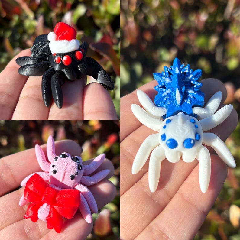 May include: Three small, 3D printed spider figurines. The first spider is black with red eyes and wears a red Santa hat. The second spider is white with blue eyes and a blue and white snowflake design. The third spider is pink with black eyes and a red bow.