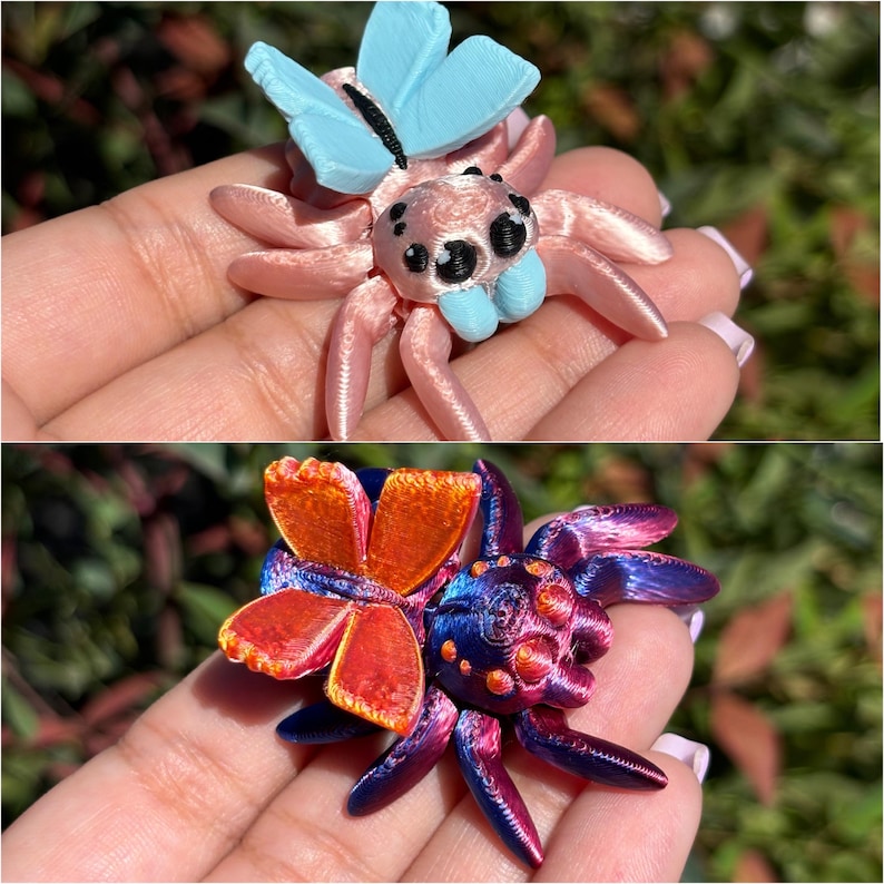 May include: Two 3D printed spider figurines with butterfly wings. The first spider is pink with blue wings and the second spider is purple with orange wings.