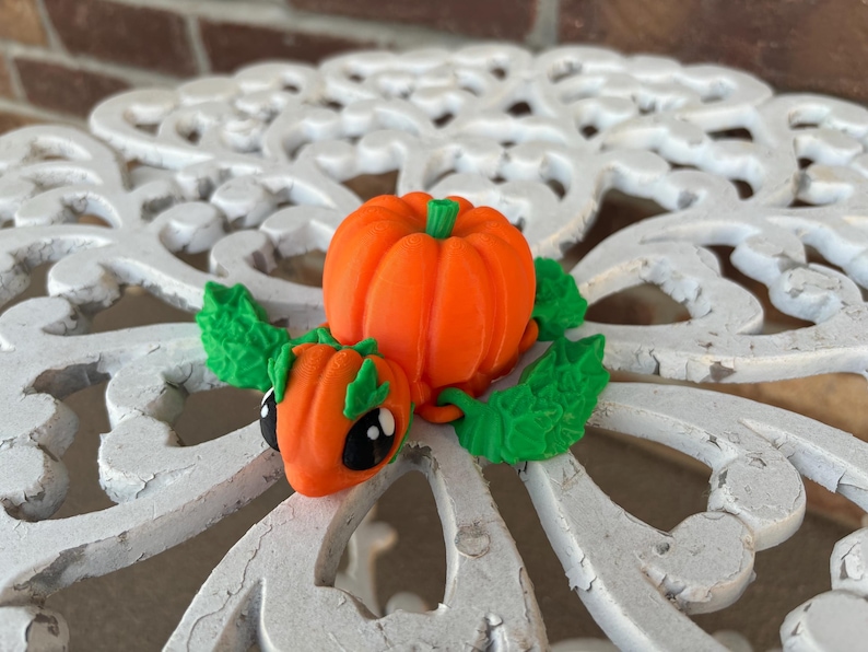May include: A small, orange pumpkin-shaped turtle figurine with green leaves. The turtle has black eyes and a cute expression.