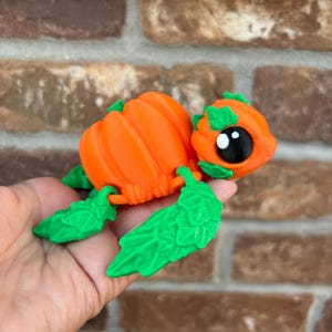May include: A small, orange pumpkin-shaped turtle figurine with green leaves for legs and a cute face.