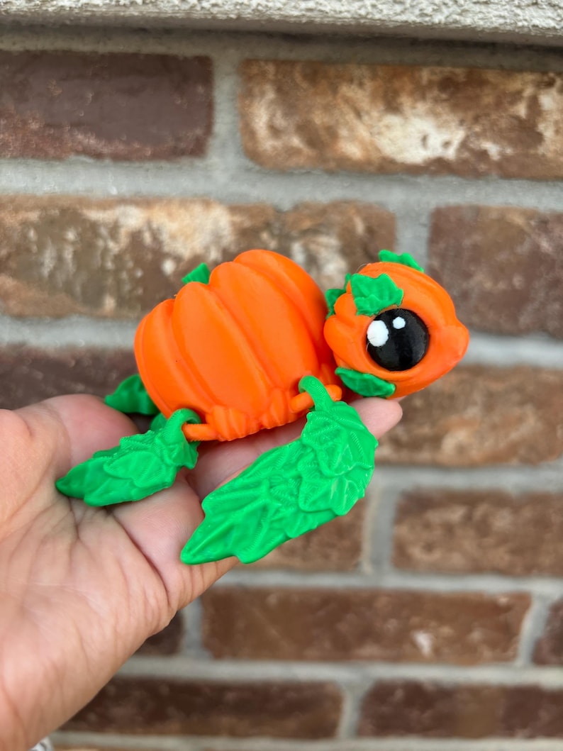 May include: A small, orange pumpkin-shaped turtle figurine with green leaves for legs and a cute face.
