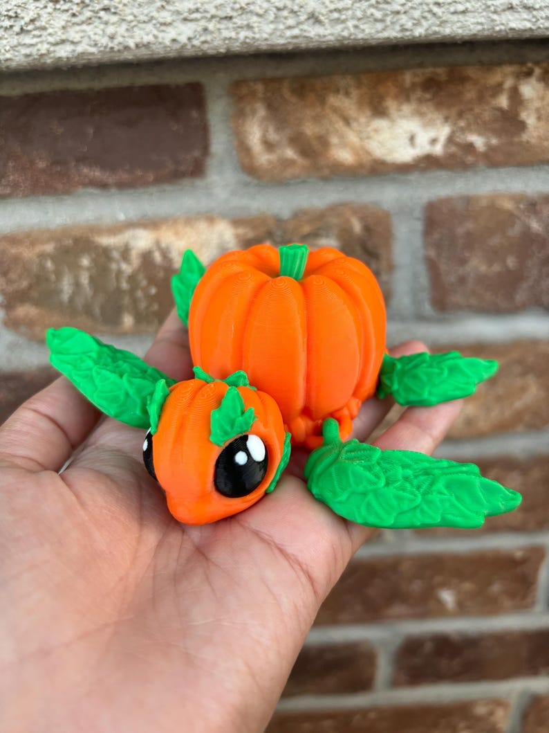 May include: A small, orange pumpkin-shaped figurine with green leaves and black eyes. The figurine is made of a smooth, plastic-like material.