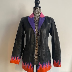 Könnte beinhalten: Eine schwarze Lederjacke mit einem lila und pinkfarbenen Kragen und orangefarbenen und lilafarbenen Flammendetails am Saum und an den Ärmeln.
