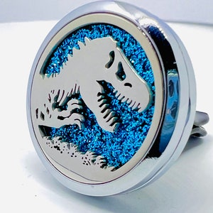 Könnte beinhalten: Ein silberner Autolufterfrischer mit einem blauen Glitzerhintergrund und einem Dinosaurierausschnitt.